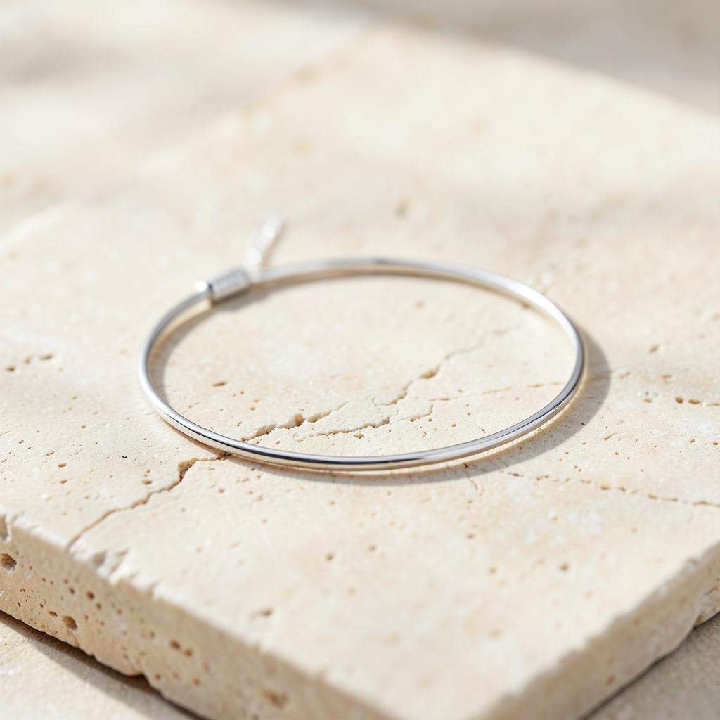 Minimal silver-tone anklet resting on a pale stone surface